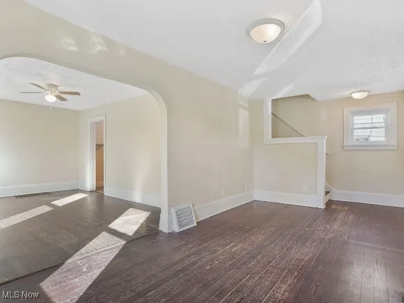 Spare room featuring dark wood-style flooring, arched walkways, a ceiling fan, and a textured ceiling