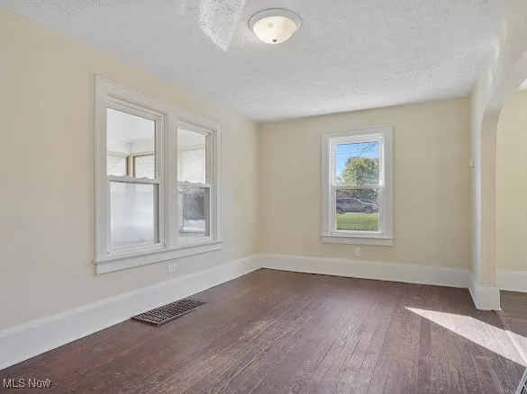 Unfurnished room with arched walkways, dark wood-style floors, and a textured ceiling