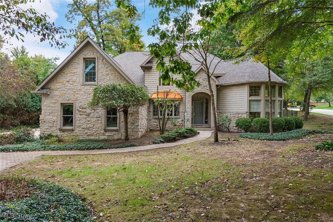 View of front of property featuring stone siding, roof with shingles, and a front yard