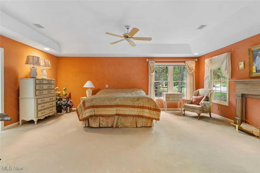 Bedroom with a tray ceiling, carpet, ceiling fan, a fireplace, and recessed lighting