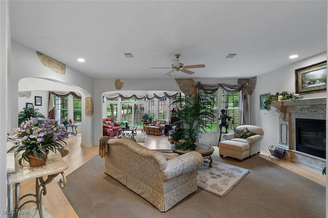 Great room featuring wood finished floors, a premium fireplace, recessed lighting, arched walkways, and ceiling fan