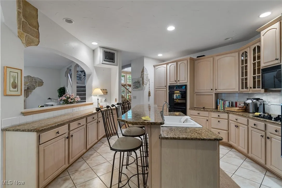 Kitchen with backsplash, glass insert cabinets, light brown cabinetry, a center island with sink, and recessed lighting
