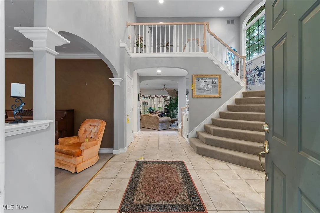 Entryway featuring arched walkways, healthy amount of natural light, stairs, light tile patterned flooring, and a towering ceiling