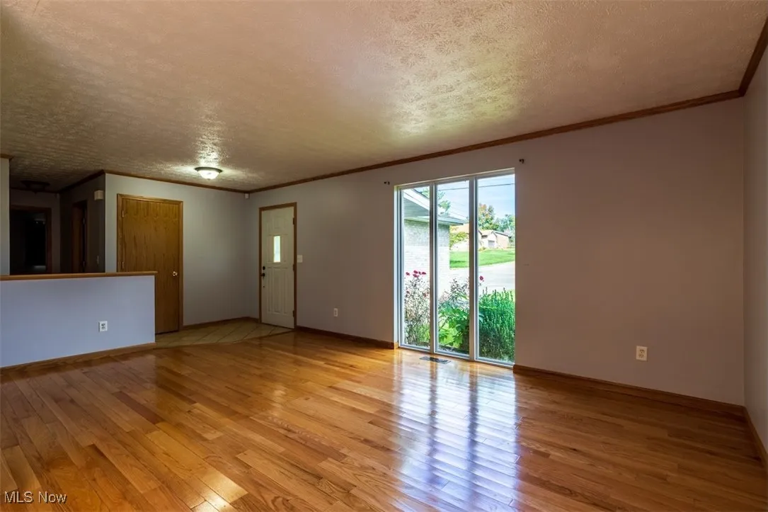 Unfurnished living room featuring ornamental molding, a textured ceiling, and light wood-style flooring