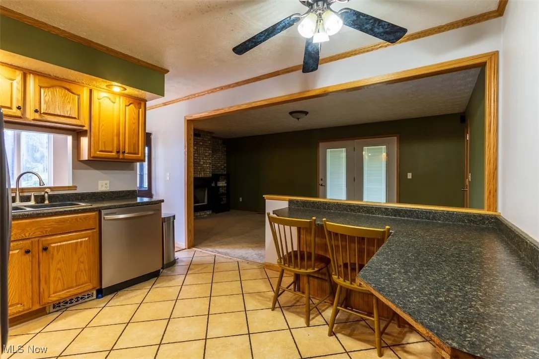 Kitchen with ornamental molding, a textured ceiling, a breakfast bar, stainless steel dishwasher, and a peninsula