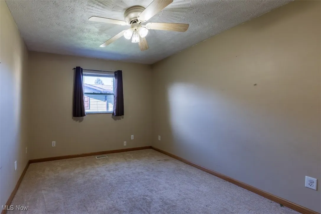 Carpeted empty room featuring a textured ceiling and ceiling fan