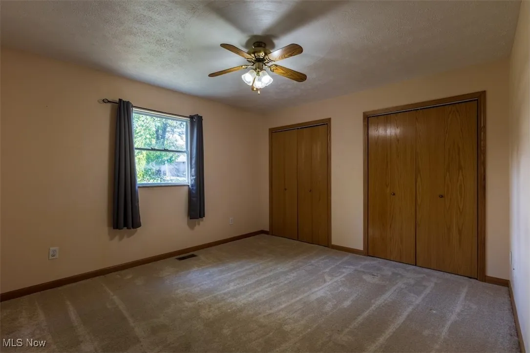 Unfurnished bedroom with multiple closets, carpet, a textured ceiling, and ceiling fan