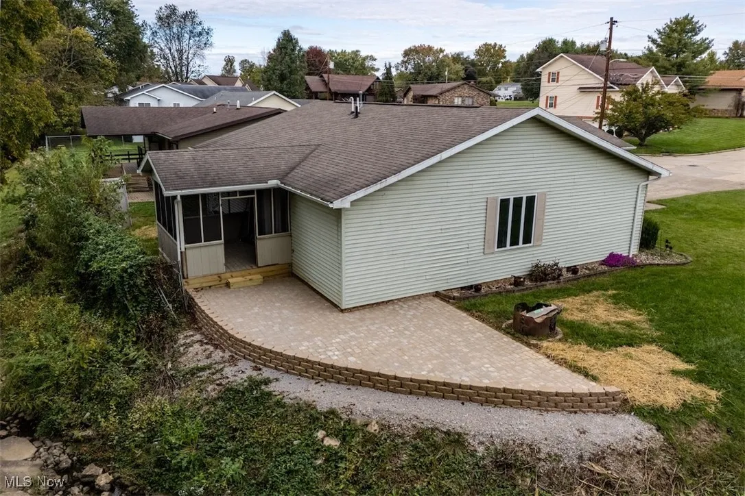 Back of property with a shingled roof, a sunroom, a lawn, and a patio area