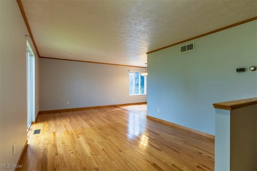 Unfurnished room featuring light wood-style flooring, crown molding, a textured ceiling, and a chandelier
