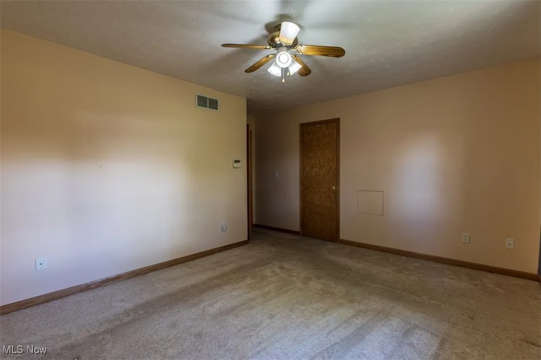 Carpeted empty room with a textured ceiling and ceiling fan