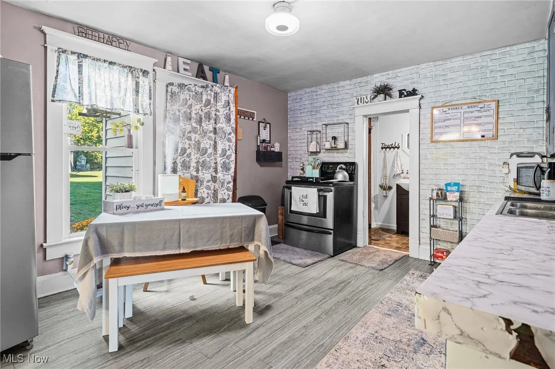 Bedroom featuring brick wall, freestanding refrigerator, and light wood-style flooring