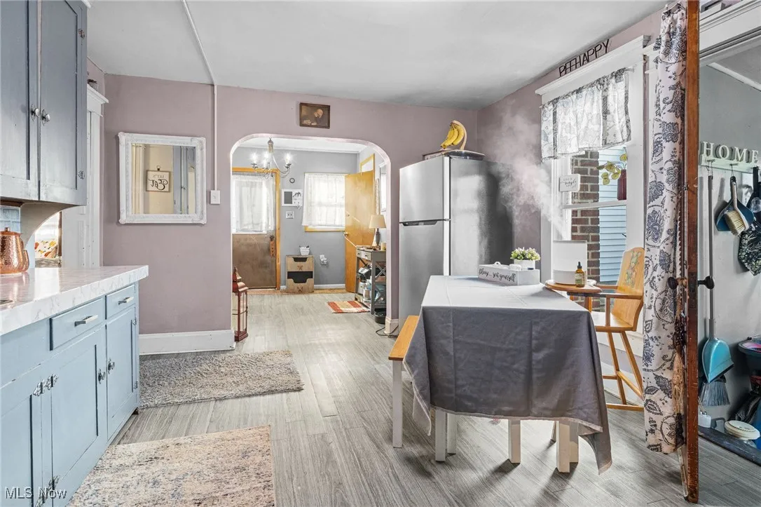 Kitchen featuring arched walkways, freestanding refrigerator, light wood-style floors, a chandelier, and blue cabinetry