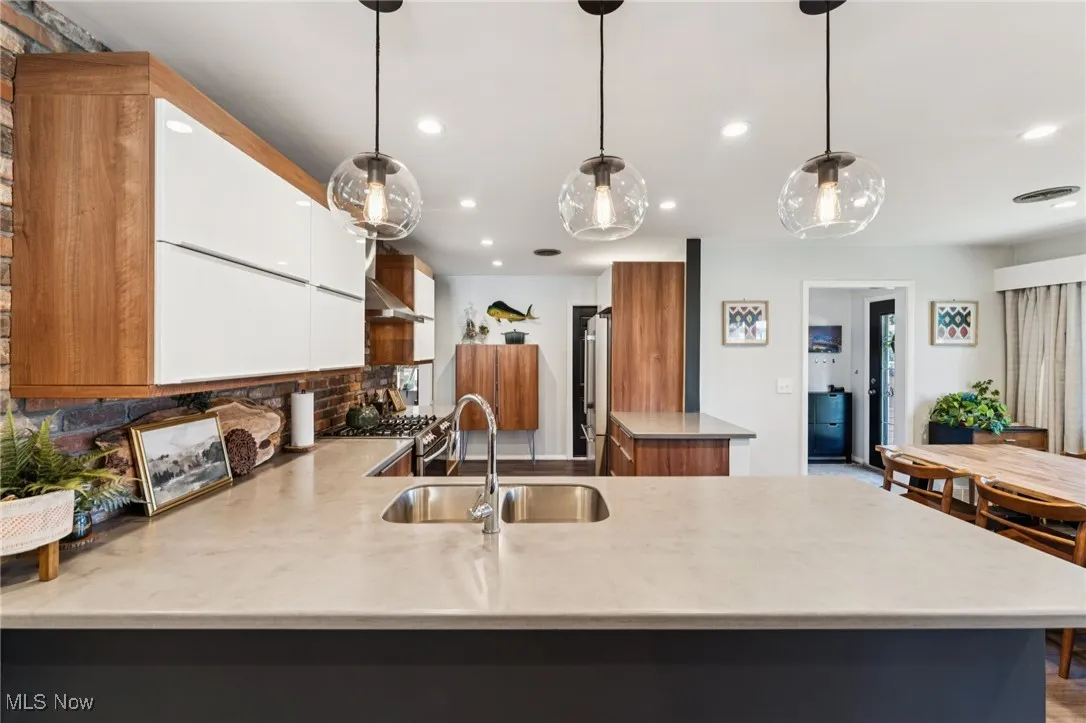 Kitchen featuring white cabinets, brown cabinetry, a peninsula, decorative light fixtures, and recessed lighting