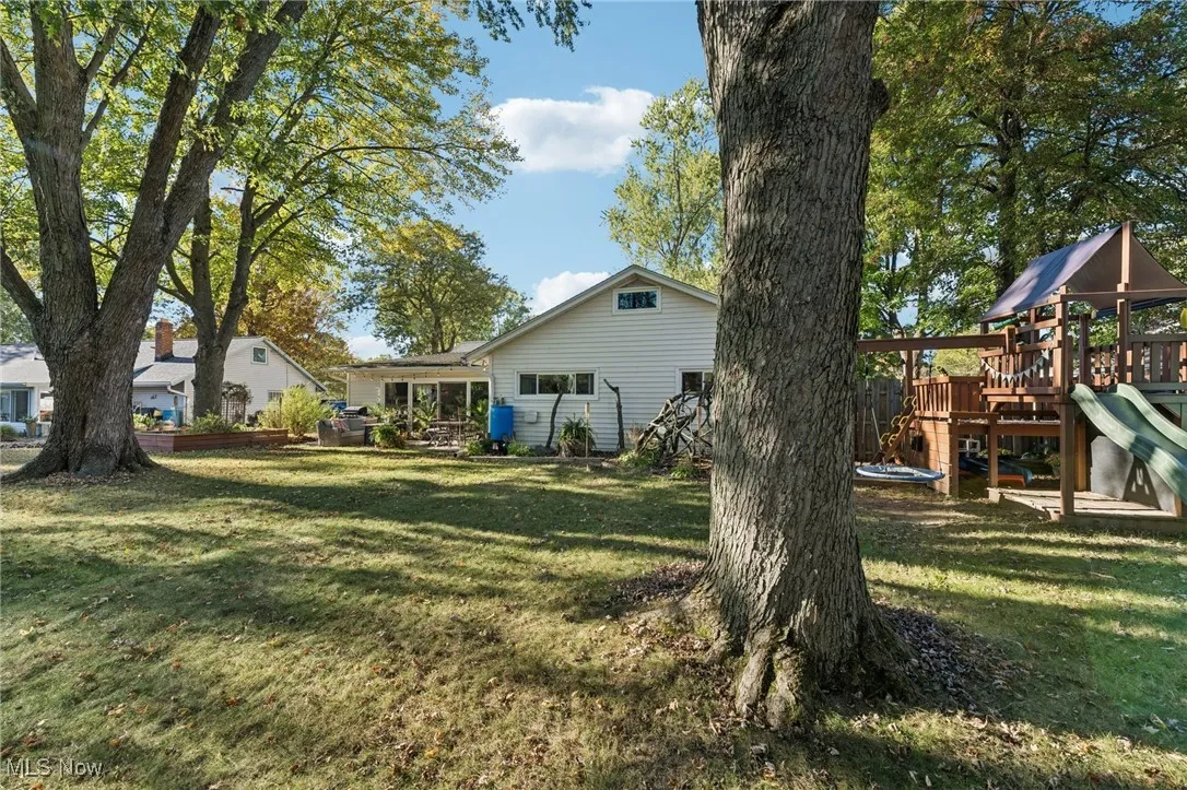 Rear view of property featuring a playground, a lawn, and a wooden deck
