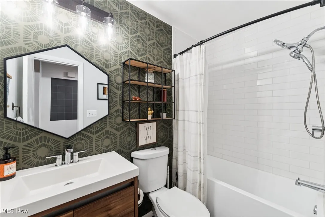 Bathroom featuring wallpapered walls, shower / bath combo with shower curtain, vanity, tile walls, and backsplash