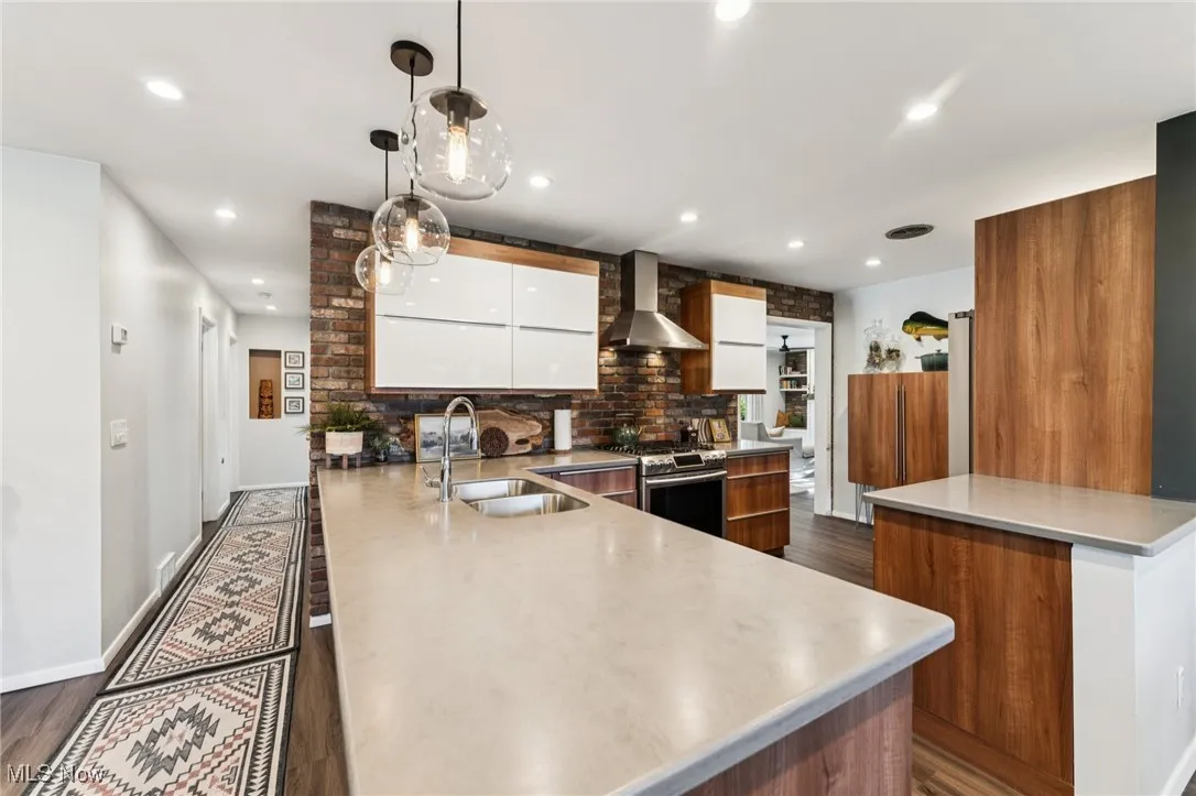 Kitchen with a peninsula, backsplash, white cabinets, wall chimney exhaust hood, and stainless steel gas stove