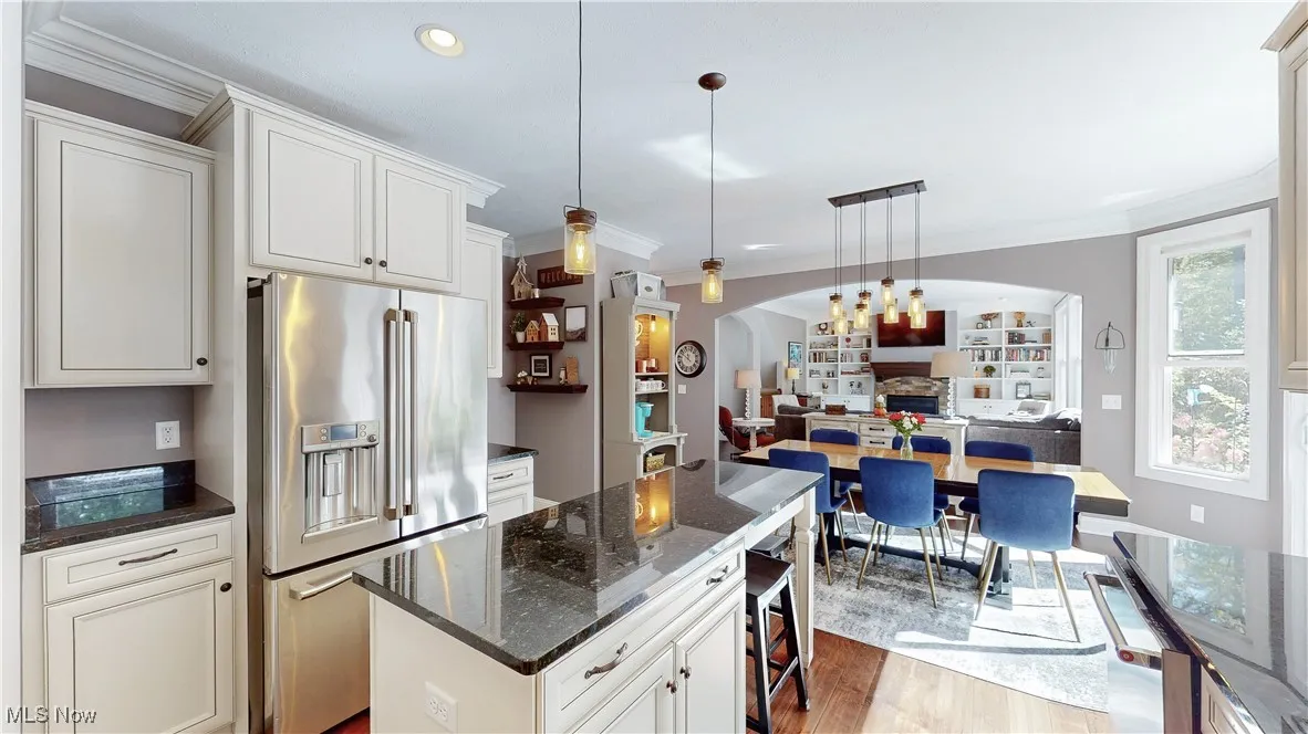 Kitchen featuring appliances with stainless steel finishes, ornamental molding, hanging light fixtures, dark stone counters, and wood finished floors