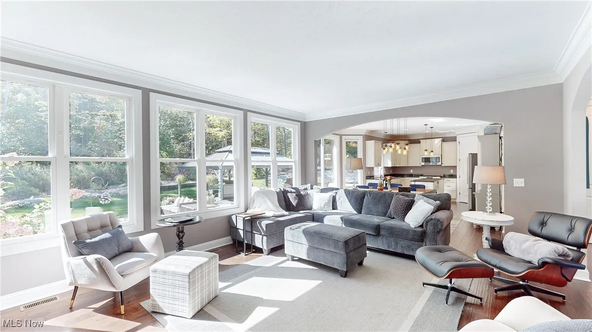 Living area with wood finished floors, arched walkways, ornamental molding, and a chandelier