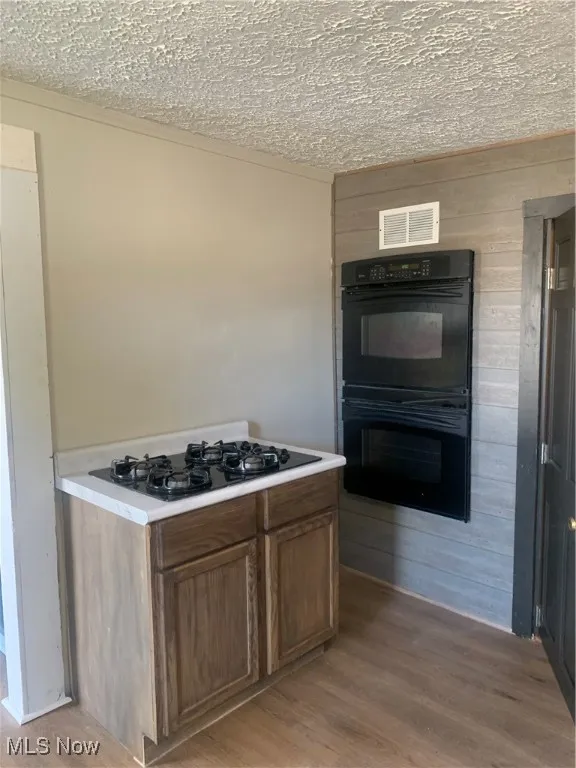 Kitchen with light wood-type flooring, wooden walls, stovetop, light countertops, and a textured ceiling