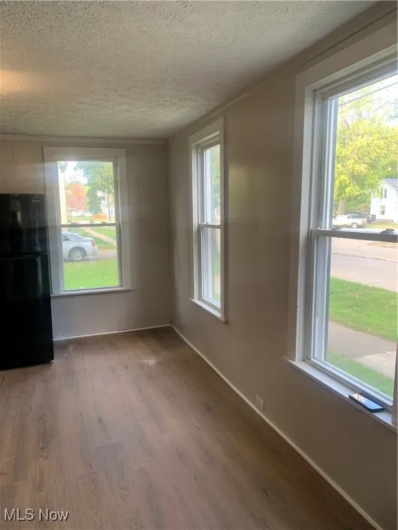 Unfurnished living room with wood finished floors, healthy amount of natural light, a textured ceiling, and ornamental molding