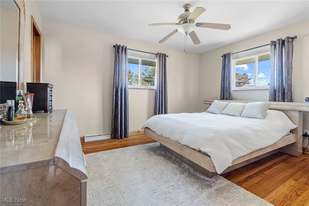 Bedroom with light wood-type flooring, ceiling fan, multiple windows, and a baseboard heating unit