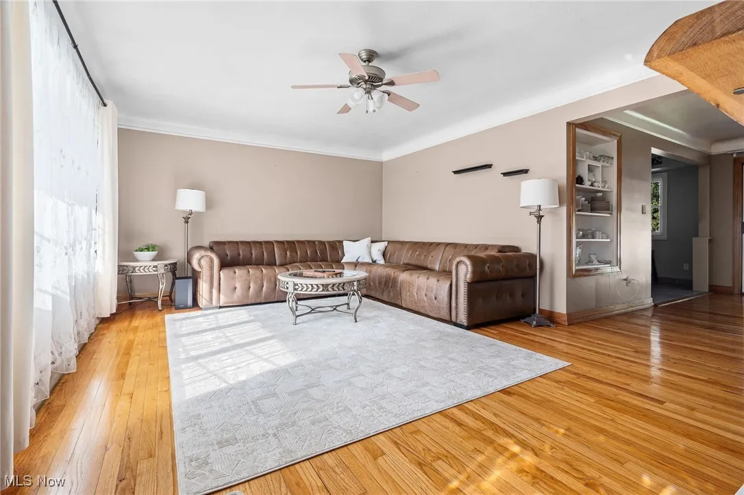 Living room with light wood-style flooring, ceiling fan, and ornamental molding