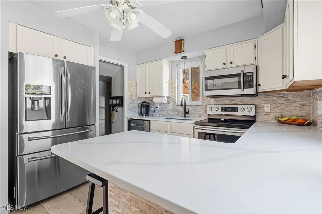 Kitchen featuring stainless steel appliances, a peninsula, light stone counters, tasteful backsplash, and light tile patterned floors