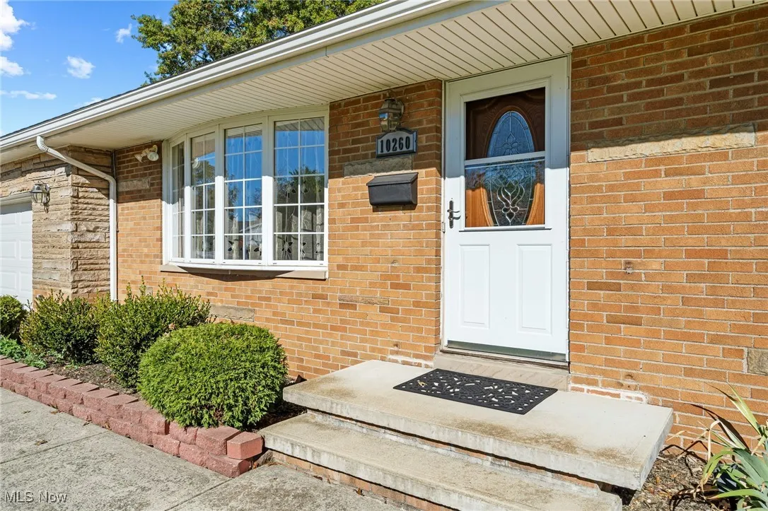 Doorway to property with brick siding, a garage, and a porch