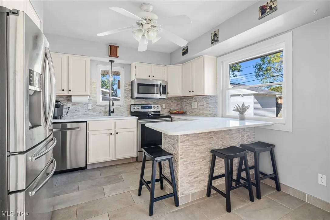 Kitchen featuring stainless steel appliances, a kitchen bar, tasteful backsplash, and a peninsula