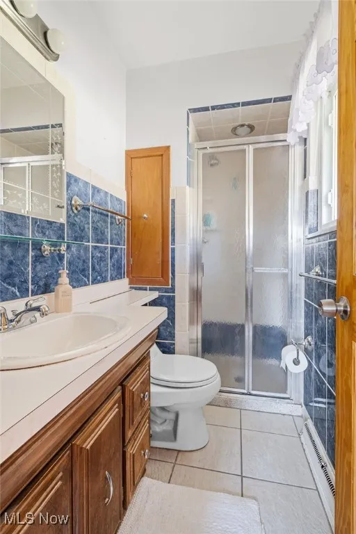 Bathroom with tile walls, vanity, light tile patterned floors, and a stall shower