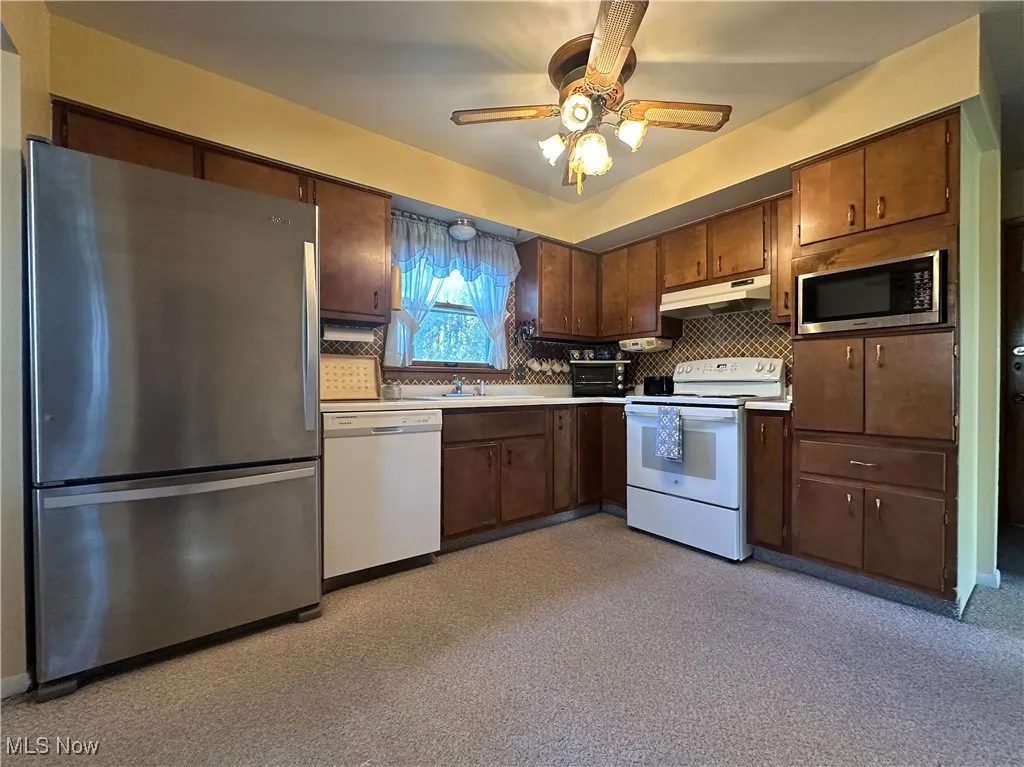 Kitchen with appliances with stainless steel finishes, light countertops, decorative backsplash, under cabinet range hood, and ceiling fan