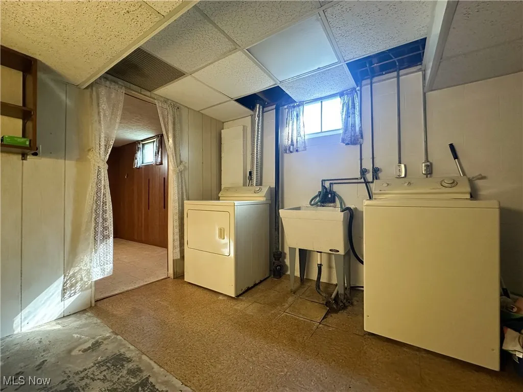 Laundry area featuring a drop ceiling, washing machine and clothes dryer, and wood walls