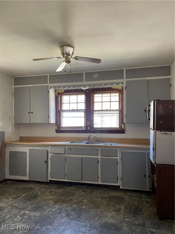 Kitchen featuring light countertops, a ceiling fan, gray cabinetry, and dark stone finish floors