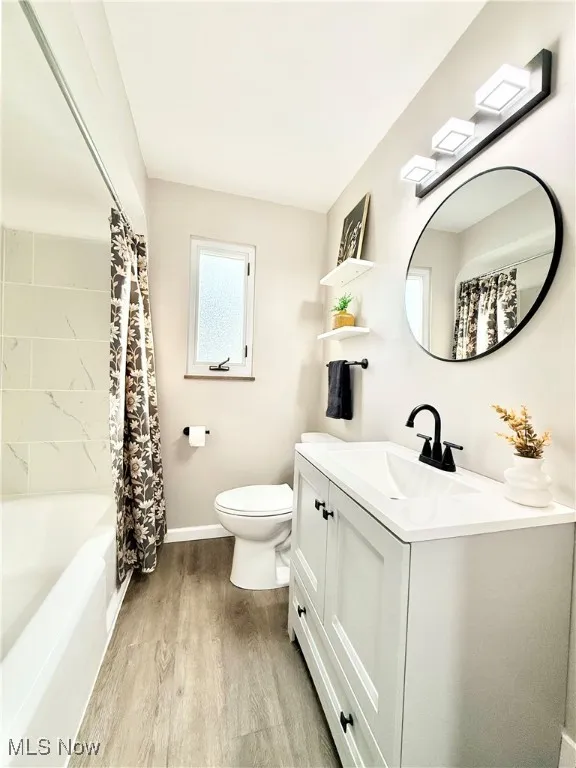 Bathroom with shower / bath combination with curtain, light wood-style floors, and vanity