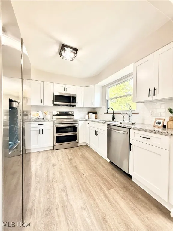 Kitchen with white cabinets, appliances with stainless steel finishes, light stone counters, and backsplash