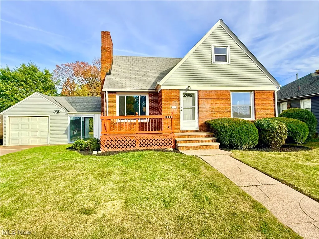 View of front of home with a front lawn, brick siding, a deck, a garage, and a shingled roof