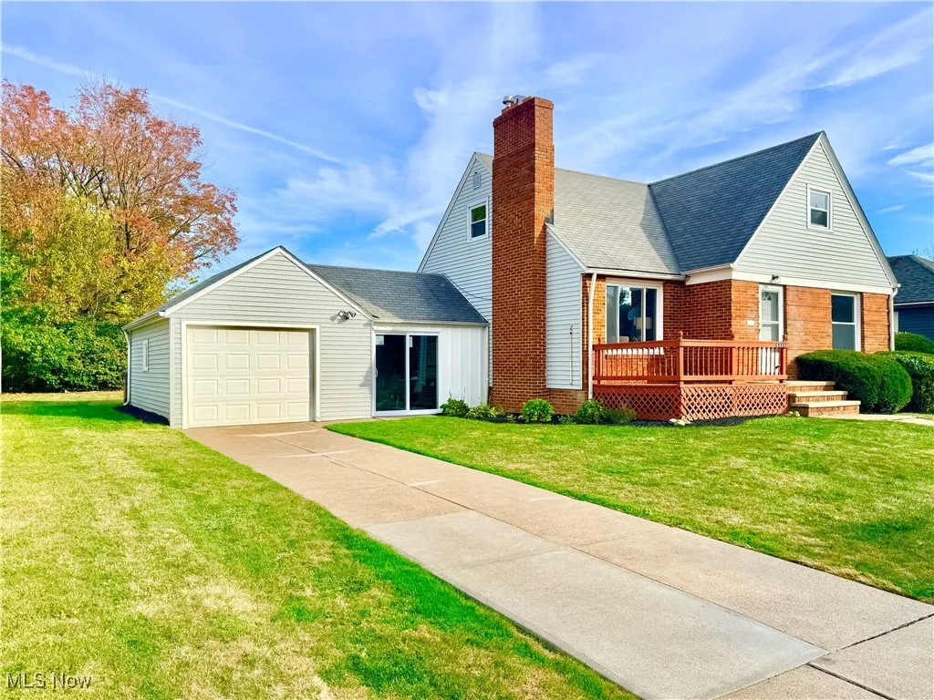 View of front facade featuring a shingled roof, brick siding, a wooden deck, and a front yard