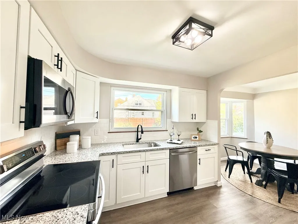 Kitchen with appliances with stainless steel finishes, white cabinets, light stone counters, and dark wood-style flooring