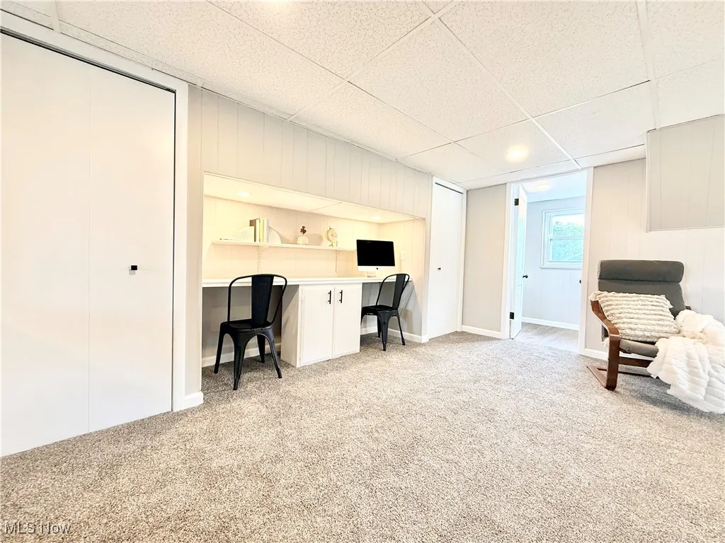 Office with a drop ceiling, built in desk, light colored carpet, and wooden walls