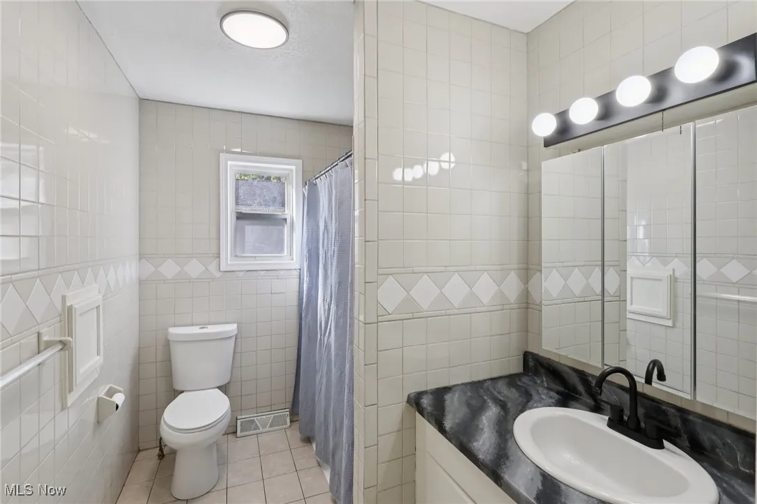 Full bathroom featuring tile walls, light tile patterned floors, vanity, and a tile shower