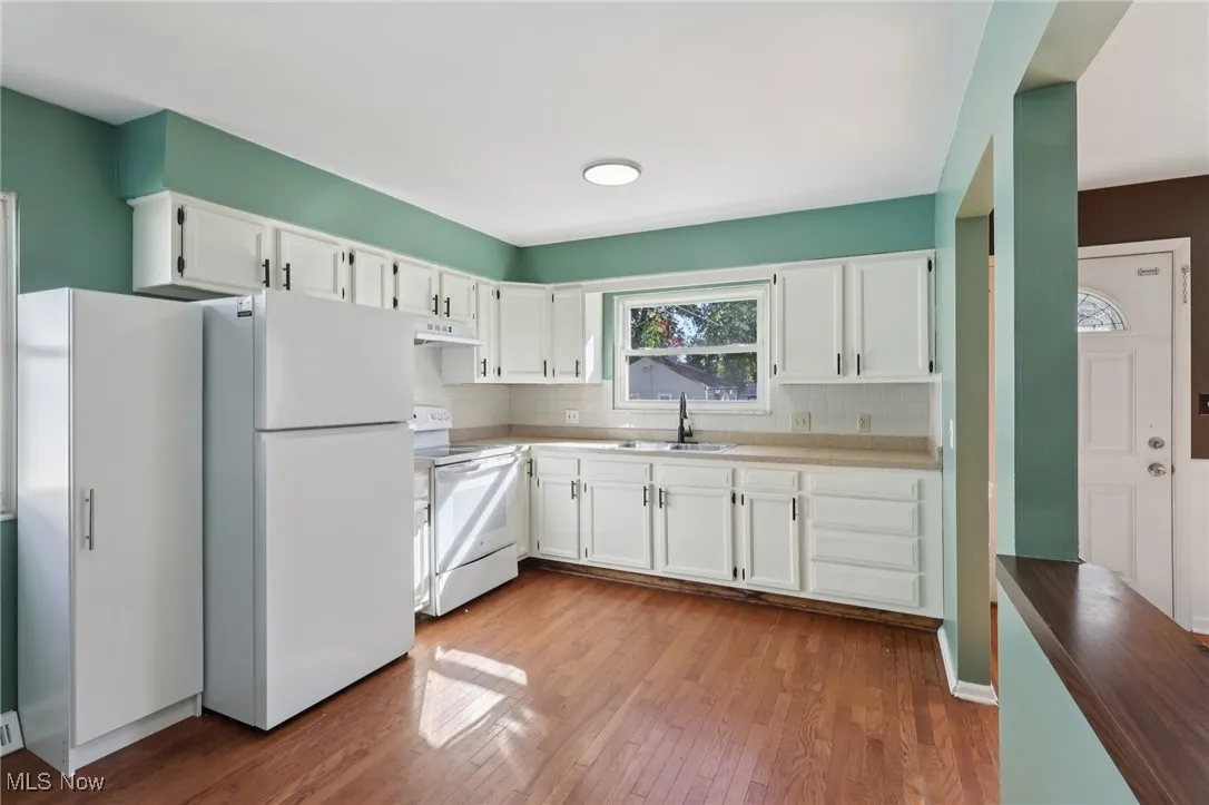 Kitchen with white cabinets, white appliances, light wood-type flooring, decorative backsplash, and light countertops