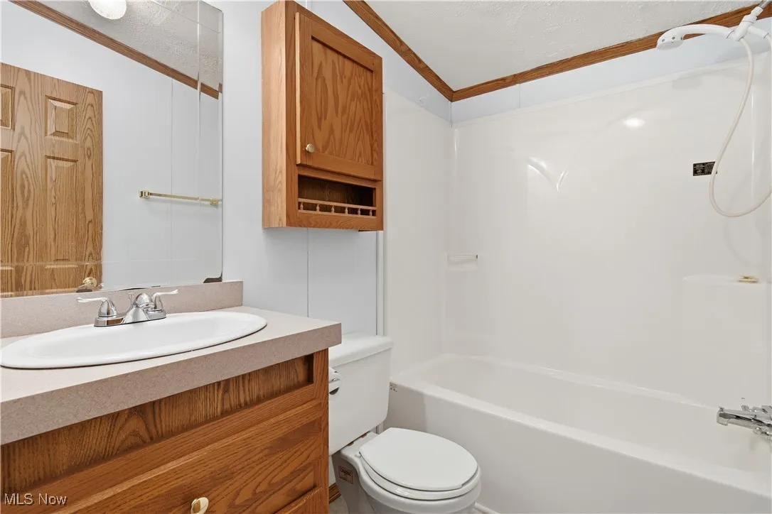 Full bath featuring vanity, bathtub / shower combination, a textured ceiling, and ornamental molding