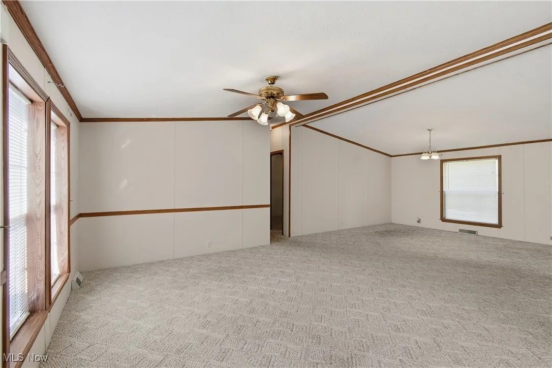 Unfurnished room featuring crown molding, light colored carpet, ceiling fan, a chandelier, and a decorative wall