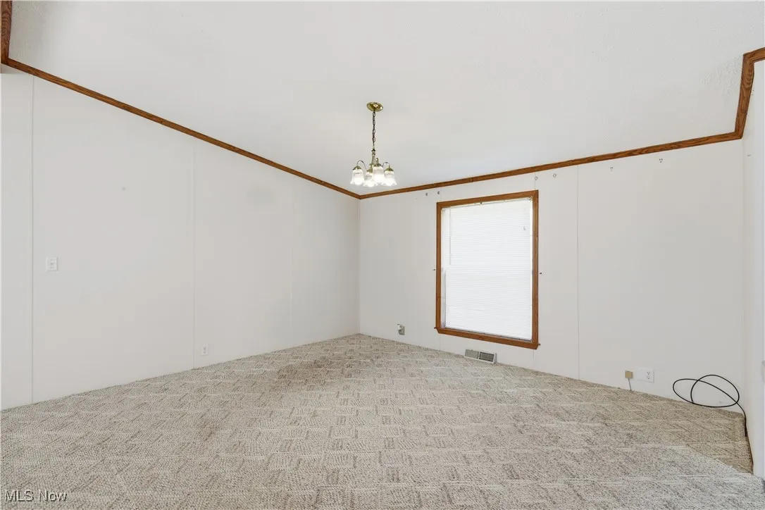 Empty room with crown molding, a chandelier, and light carpet