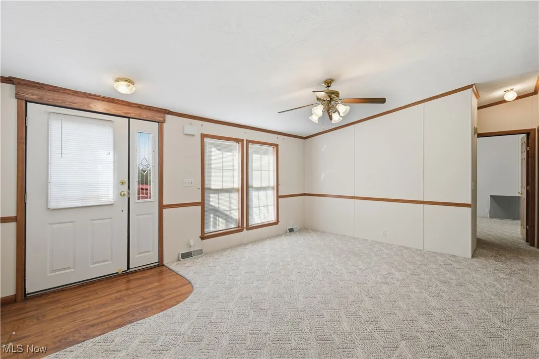 Foyer featuring ornamental molding, light colored carpet, ceiling fan, and light wood finished floors