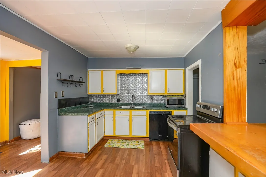 Kitchen with stainless steel appliances, white cabinetry, decorative backsplash, and wood-style floors