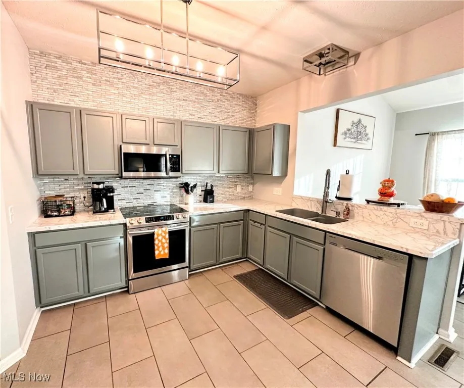 Kitchen featuring gray cabinetry, tasteful backsplash, stainless steel appliances, light stone counters, and light tile patterned flooring