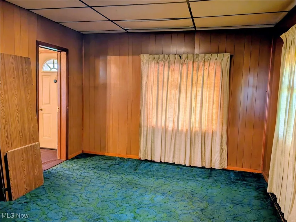 Carpeted empty room with wood walls and a drop ceiling