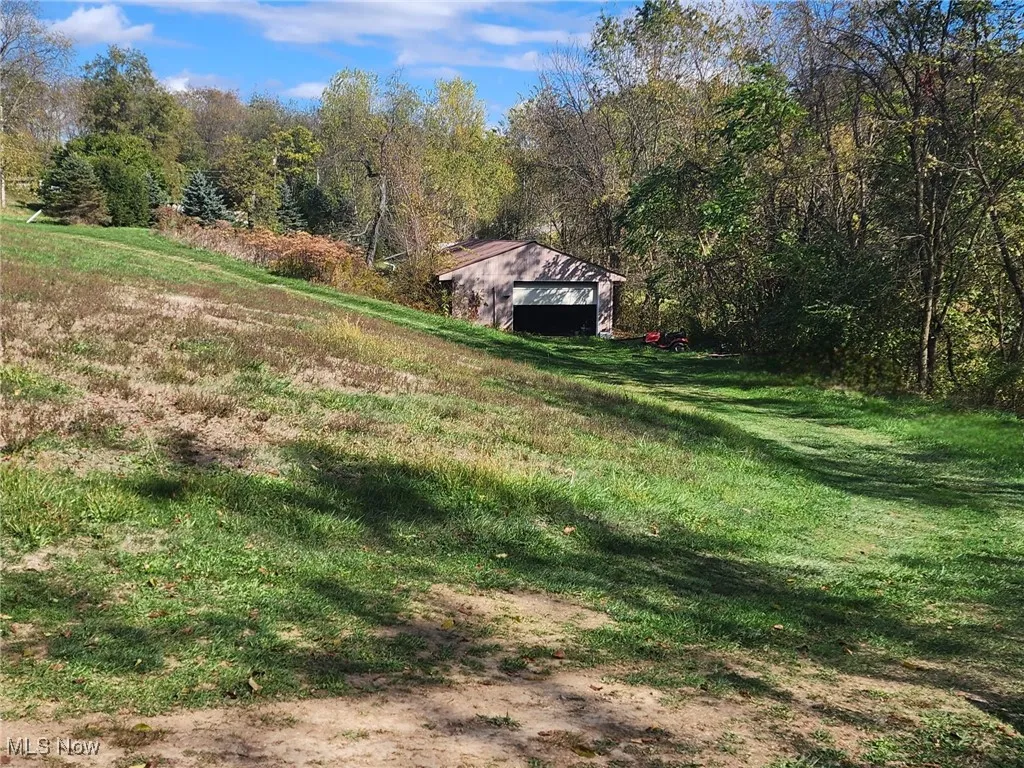 View of grassy yard featuring a wooded view and an outdoor structure