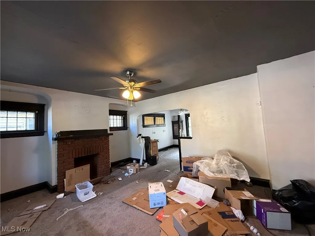 Living area with a fireplace, arched walkways, carpet, and ceiling fan